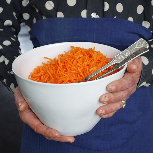 gros plan sur un saladier en porcelaine blanche de forme irrégulière rempli de carottes rapés et tenu en main - tsé tsé
