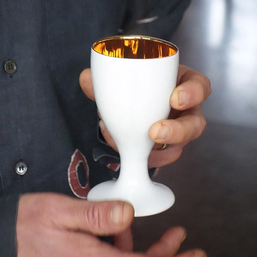 des mains tiennent un verre blanc et or - tsé tsé