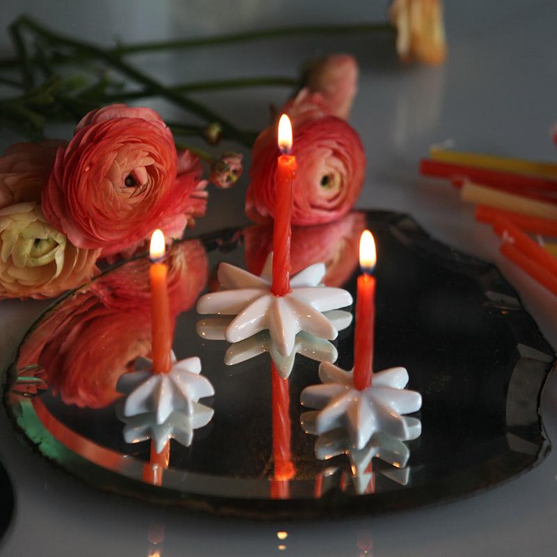 bougies d'anniversaire rouges sur des petits bougeoirs étoilés en porcelaine blanche et renoncules en arrière plan - tsé tsé