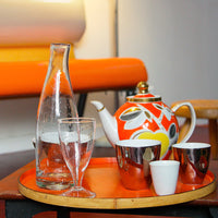 carafe et verre à pied en verre incrusté de petites bulles sur un plateau rond orange - tsé tsé
