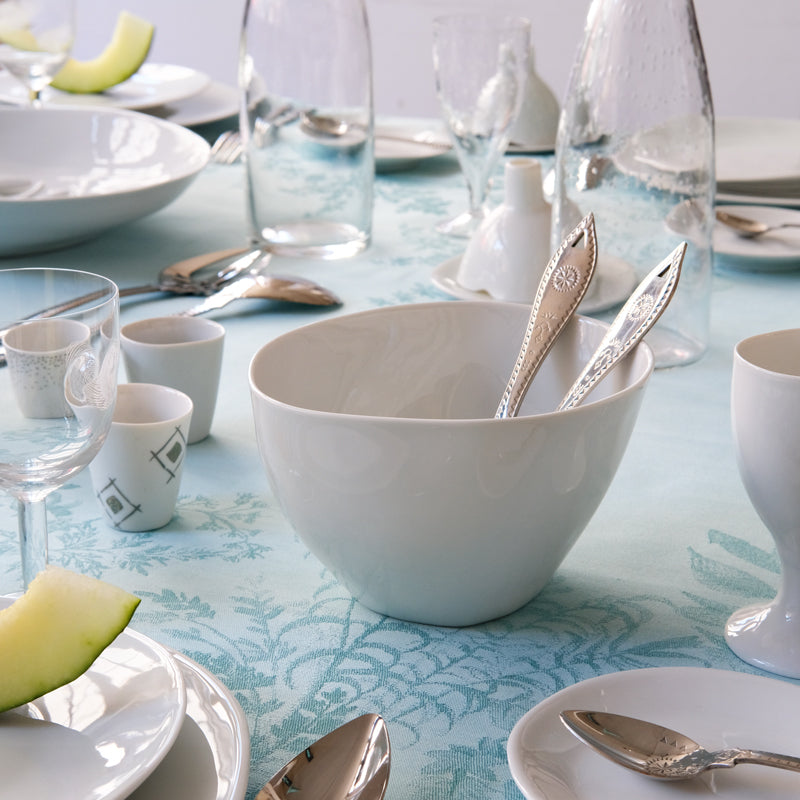 Petit saladier blanc de forme irrégulière avec couverts à salade à l'intérieur, au milieu d'une table dréssée. 