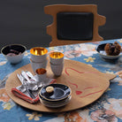 Plateau en bois avec vaisselle, posés sur une table avec nappe fleurie.