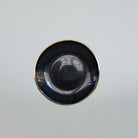 Soucoupe de forme irrégulière, noire avec bordure or. Tsé & Tsé