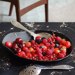 grande assiette nore de forme asymétrique partiellement émaillée et remplie de fruits rouges - tsé tsé