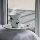 tasse à expresso et soucoupe blanc et argent devant une fenêtre - tsé tsé