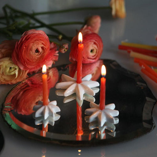 bougies d'anniversaire rouges sur des petits bougeoirs étoilés en porcelaine blanche et renoncules en arrière plan - tsé tsé