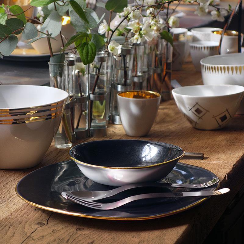 coupelle et assiette en porcelaine sombre bleutée avec un liseré or avec un vase d'avril en arrière plan - tsé tsé