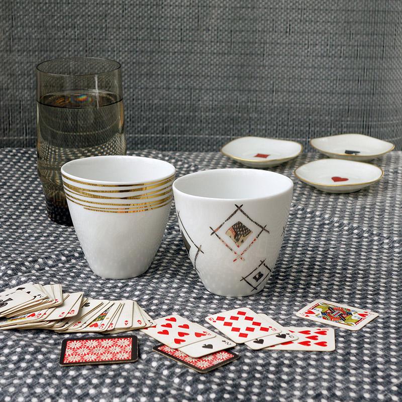tasses or et argent et derrière un jeu de carte éparpillé sur une table - tsé tsé